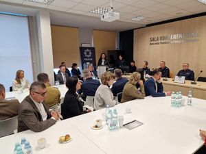 widok na salę konferencyjną , w której znajdują się osoby w ubraniu cywilnym i w mundurach, jedna osoba stoi przy mównicy.