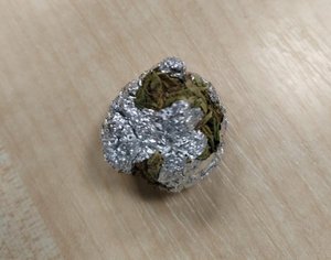 zawiniątko folii aluminiowej i suszu roślinnego w kolorze ciemnozielonym.