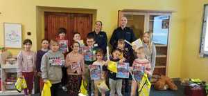 policjantka i policjant razem z dziećmi  trzymają w rękach ulotki z motywem walentynkowym, na nim widoczne logo komendy policji w Opocznie.