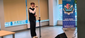 chłopiec trzyma mikrofon, stoi na sali, w tle napis komenda powiatowa policji w Opocznie.