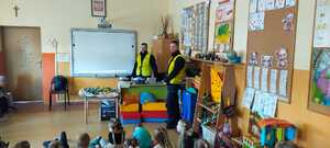 policjanci w odblaskowych kamizelkach, w klasie szkolnej rozmawiają z dziećmi.