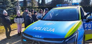 dzieci ubrane w kurtki znajdują się na dworze przy radiowozie policyjnym.