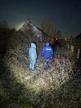 policjant z osobą w długiej kurtce w wieczornej porze znajduje się przed opuszczonym budynkiem.