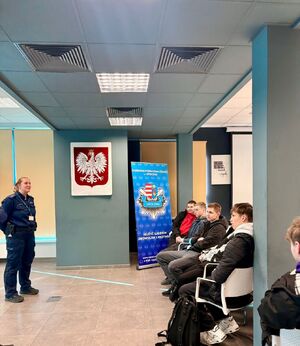 policjantka stoi przed grupą młodzieży siedzącej w sali komendy policji.