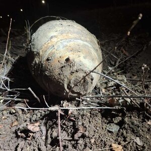 przedmiot przypominający pocisk, ubrudzony w ziemi leży na trawie.