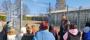 mężczyzna rozmawia z dziećmi, w tle siatka ogrodzeniowa.