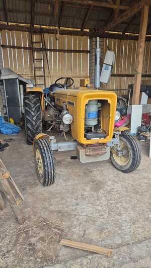 ciągnik w kolorze pomarańczowym, w tle drewniana budowla.