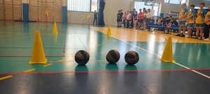 sala gimnastyczna, pachołek, trzy piłki w tle dzieci.