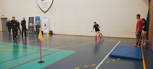 sala gimnastyczna, dzieci w strojach sportowych, policjanci, jedna osoba biegnie.