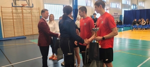 mężczyzna i policjantka stoją przed dziećmi w czerwonych strojach sportowych na sali gimnastycznej.