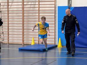 chłopiec biegnie na sali gimnastycznej obok stoi policjant.