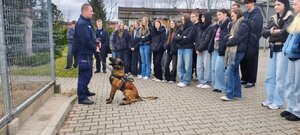 policjant z psem służbowym stoi przed grupą młodzieży.