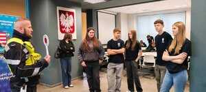 policjant w odblaskowej kamizelce rozmawia z młodzieżą na sli, pokazuje tarczę do zatrzymywania pojazdów.