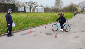 POLICJANT STOI PRZY DZIECKU JADĄCYM NA ROWERZE.