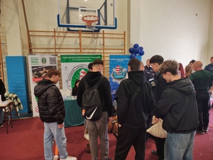 grupa młodzieży stoi wokół psa, za nimi baner Komendy Powiatowej Policji w Opocznie.