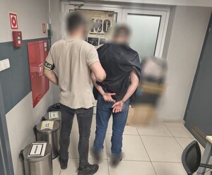 dwóch mężczyzn, jeden z napisem na ręku policja, drugi trzyma ręce z tyłu w kajdankach.