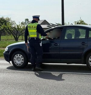 policjant w odblaskowej kamizelce stoi na drodze przy samochodzie z urządzeniem do badania trzeźwości.