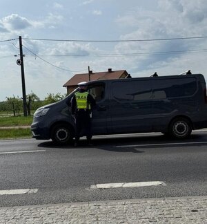 policjant w kamizelce odblaskowej stoi na drodze przy samochodzie dostawczym, w ręku trzyma urządzenie do badania trzeźwości.