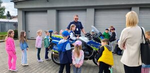 dzieci i policjant oraz kobieta stoją przy motocyklu, na którym siedzi dziewczynka.