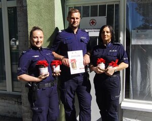 policjantki i policjant stoją ze słoikami wypełnionymi groszami, w ręku trzyma dyplom.