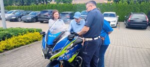 chłopiec siedzi na motocyklu policyjnym, obok stoi policjant i kobieta.