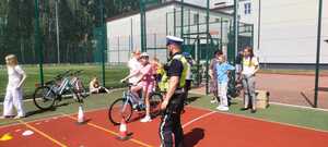 policjant w odblaskowej kamizelce na boisku razem z dzieckiem jadącym na rowerze.