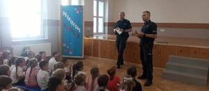 dwóch policjantów stoją przed dziećmi, za nimi napis bezpieczne wakacje.