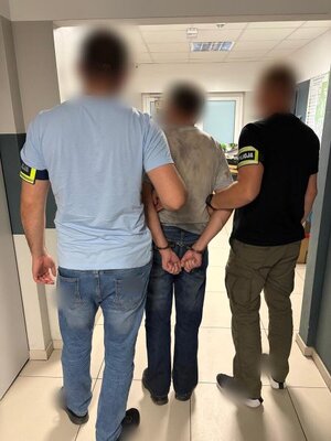 dwóch mężczyzn z opaskami z napisem policja prowadzi mężczyznę w kajdankach.