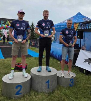 trzech mężczyzn w strojach sportowych stoi na podium.