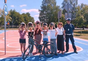 na zdjęciu widoczne miasteczko ruchu drogowego, na którym stoją dzieci z kobietą oraz umundurowany policjant, przed nimi rower.