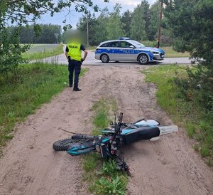 policjant idzie w kierunku radiowozu, na drodze leśnej leży motocykl.