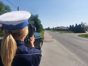 policjantka w białej czapce mierzy prędkość na drodze.
