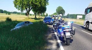 na drodze stoją radiowóz policyjny, dwa motocykle policyjne, w rowie samochód w kolorze srebrnym.