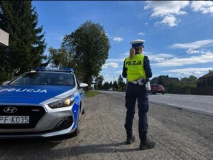 policjantka stoi obok radiowozu, obok droga.