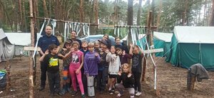 dzieci stoją razem z policjantami w lesie, za nimi namioty.