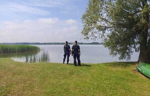 policjanci stoją nad brzegiem zbiornika wodnego.