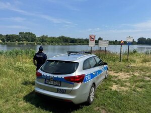 radiowóz i policjantka stoją nad brzegiem wodnego zbiornika.