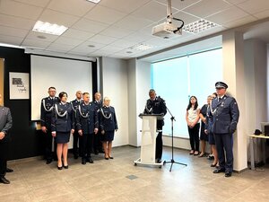 policjant przemawia z mównicy, wokół policjanci i osoby cywilne.
