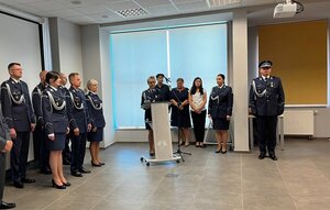 policjant przemawia z mównicy, wokół policjanci i osoby cywilne.