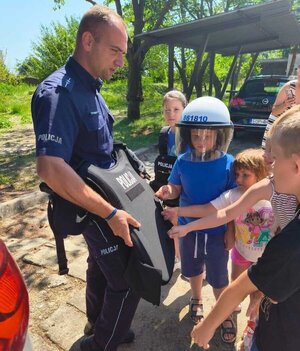 policjant pokazuje dzieciom kamizelkę.