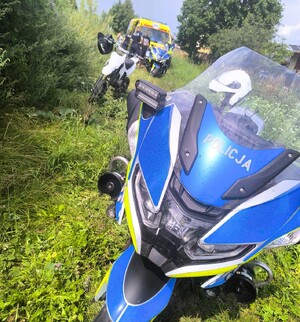 motocykl stoi na trawie, w tle biały motocykl, karetka i kilka osób, w tym policjanci.