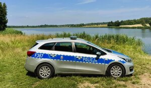 radiowóz stoi przy zbiorniku wodnym, na trawie.
