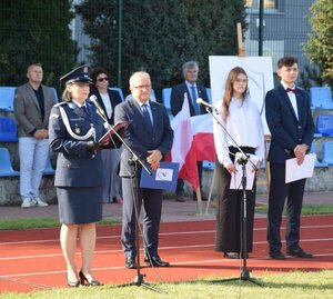 policjantka stoi przy mikrofonie, obok mężczyźni i kobiety.