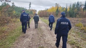 policjanci i kilka osób idą drogą w lesie.