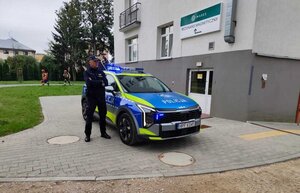 policjant stoi przed radiowozem, za nim budynek.